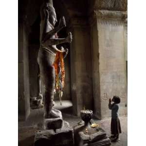 Young Girl Prays at the Foot of a Statue in Angkor Wat Temple Complex 